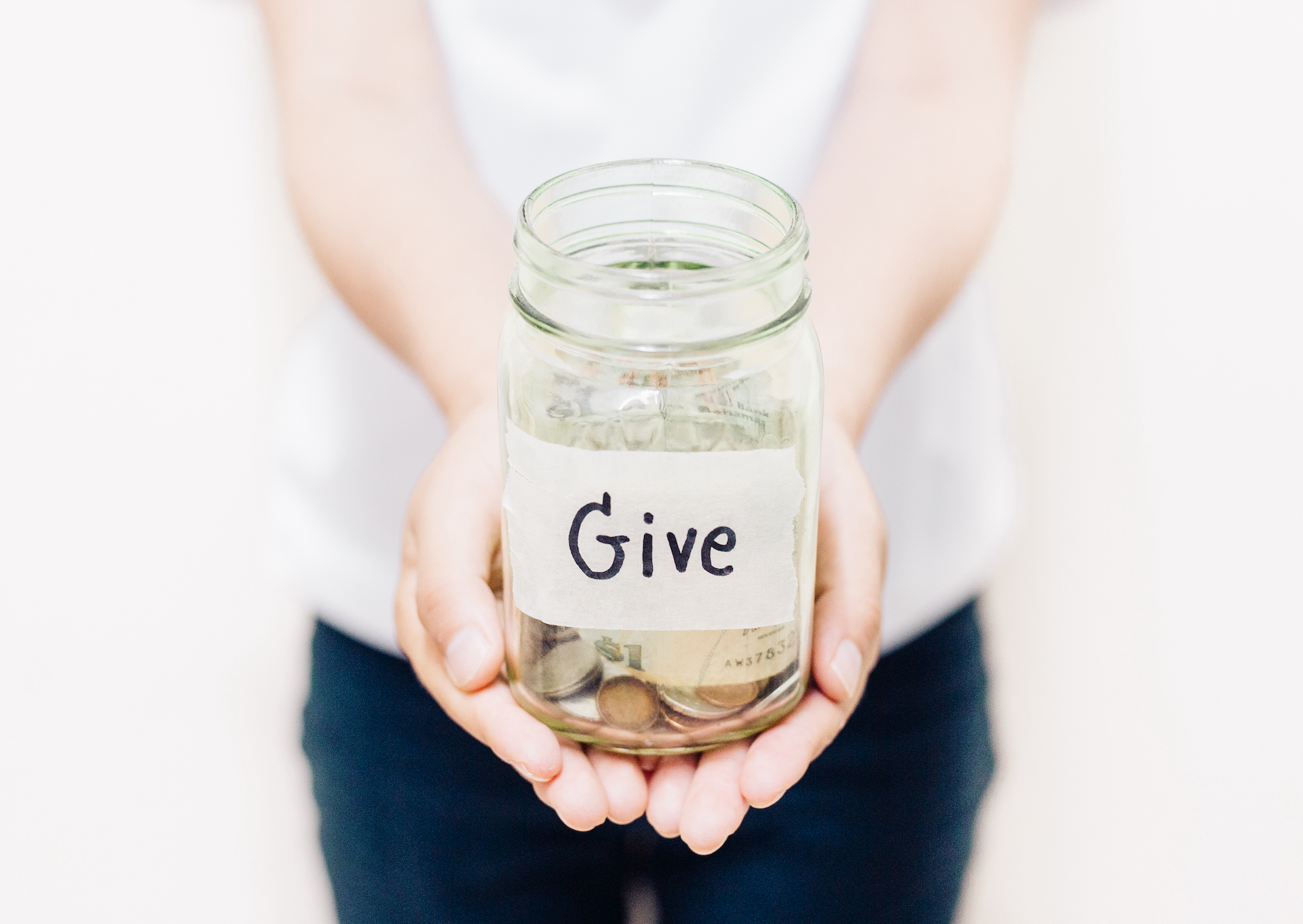 Woman holding a glass Jar with money inside and Give written on the outside.